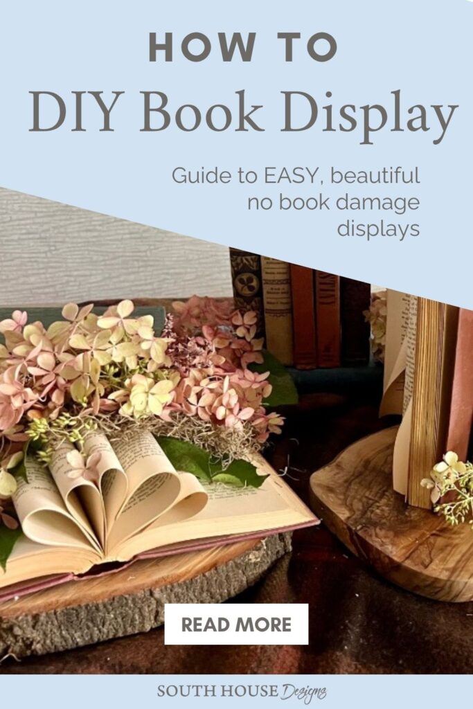 A decorative book centerpiece display with open and closed books arranged on a table, accented with dried hydrangea flowers. The text reads: “How to DIY Book Display. Guide to easy, beautiful no book damage displays. Read more. South House Designs.”.