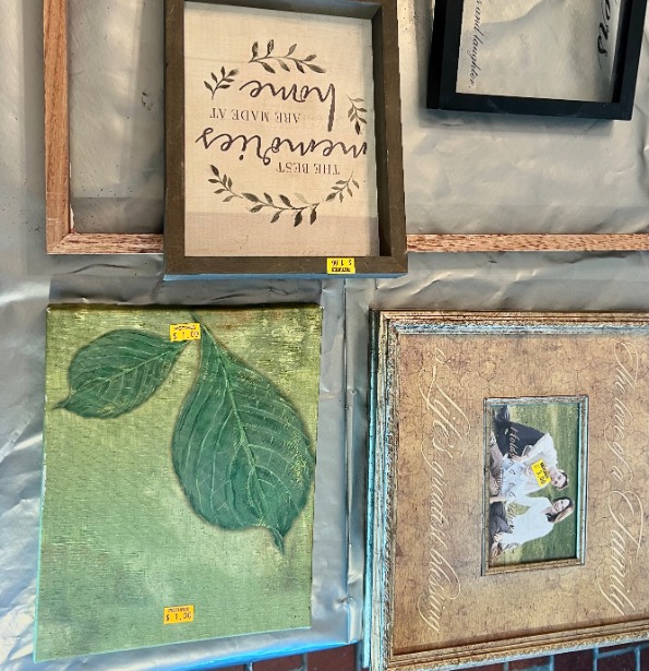 Four picture frames are displayed on a table: one with a quote about family, one empty, one with green leaves, and one with a family photo. Three have yellow price stickers.