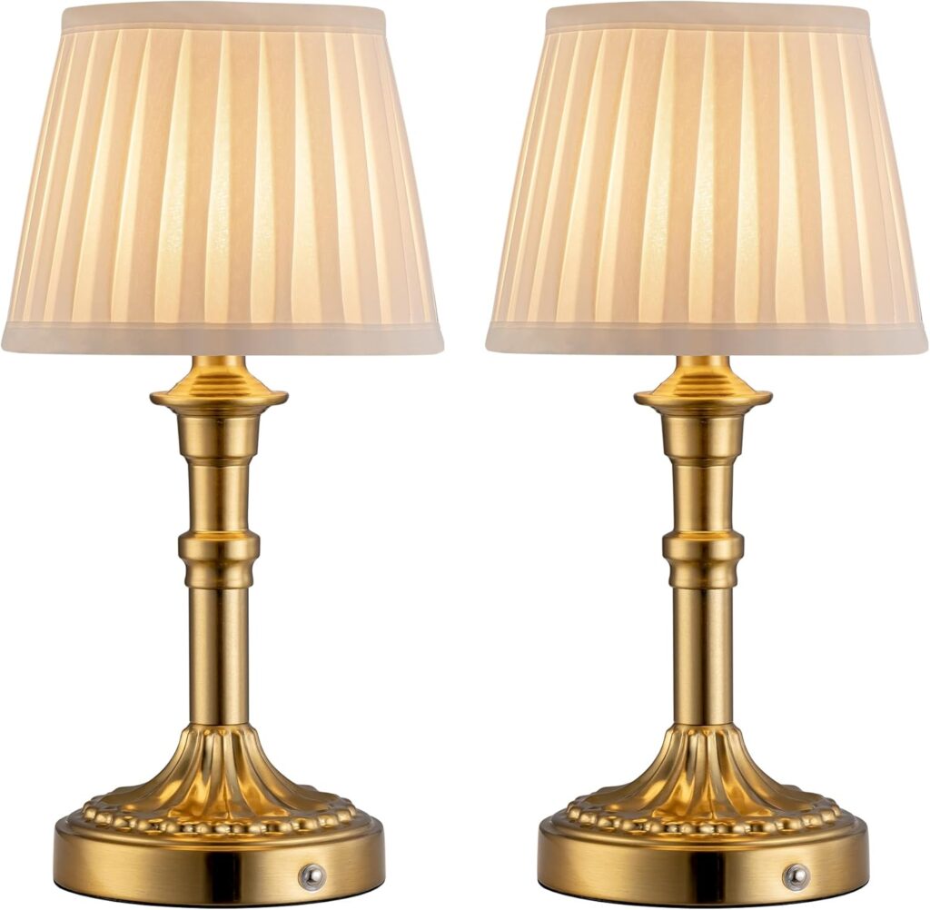 Two identical gold table lamps with pleated beige lampshades, each featuring a round base and a decorative stem. The lamps have a traditional, elegant design and are placed side by side against a white background.