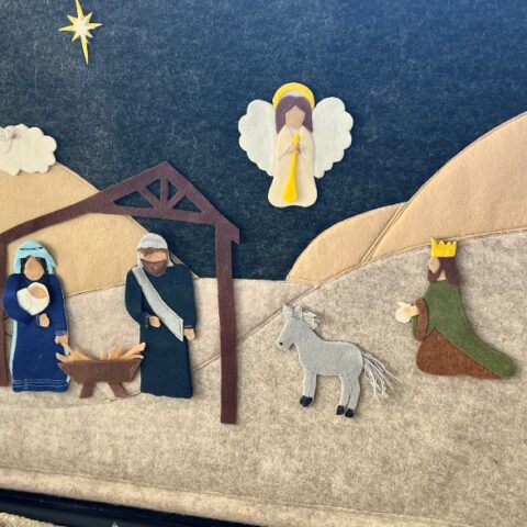 Felt board nativity scene with Mary, Joseph, and baby Jesus in a manger under a stable, a donkey, a kneeling wise man, an angel above, and the Star of Bethlehem in the night sky.