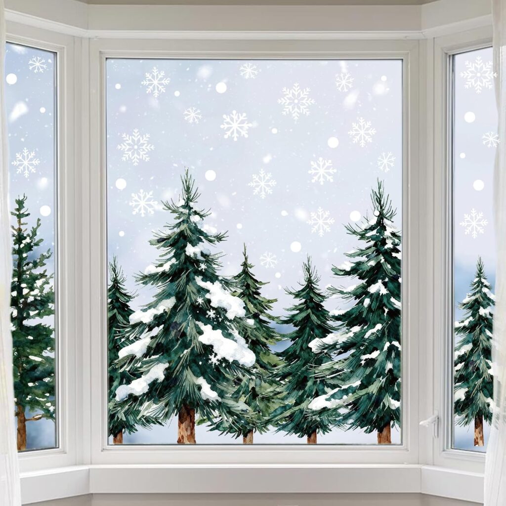 A snowy winter scene viewed through bay windows, showing tall evergreen trees with snow-covered branches and falling snowflakes against a pale, cloudy sky. White curtains frame the sides of the windows.