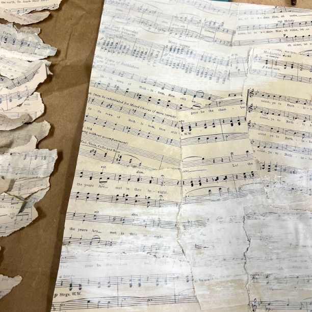 A close-up of torn and aged sheet music pages, some with visible staves and musical notes, spread out on a textured surface. The pages are yellowed and worn, showing signs of age and damage.