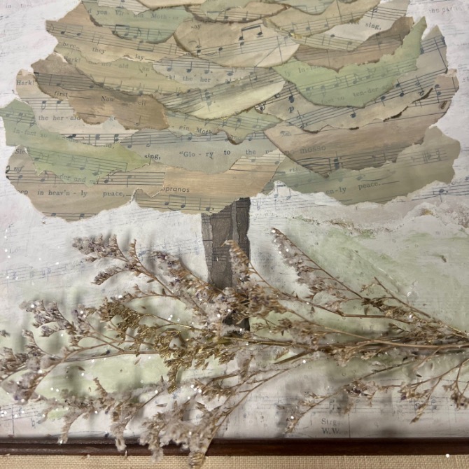 A collage of a tree made from layered pieces of sheet music forms the leaves and trunk, with dried branches and flowers placed at the base against a textured background.