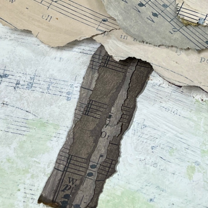 A close-up of torn pieces of sheet music layered over textured, pale paper. The musical notes and staff lines are visible on the fragments, creating an abstract collage effect.