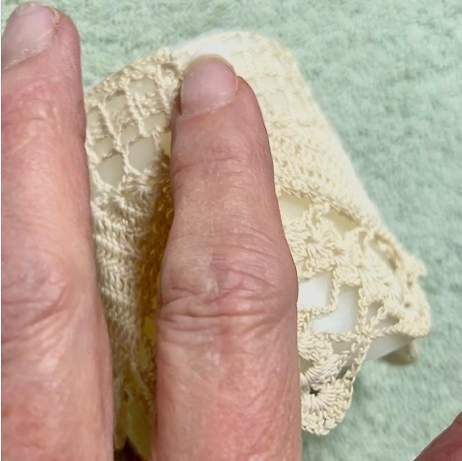 A close-up of two fingers resting on a light green textured fabric, next to beige crocheted lace—perfect inspiration for your next DIY lace candles project.