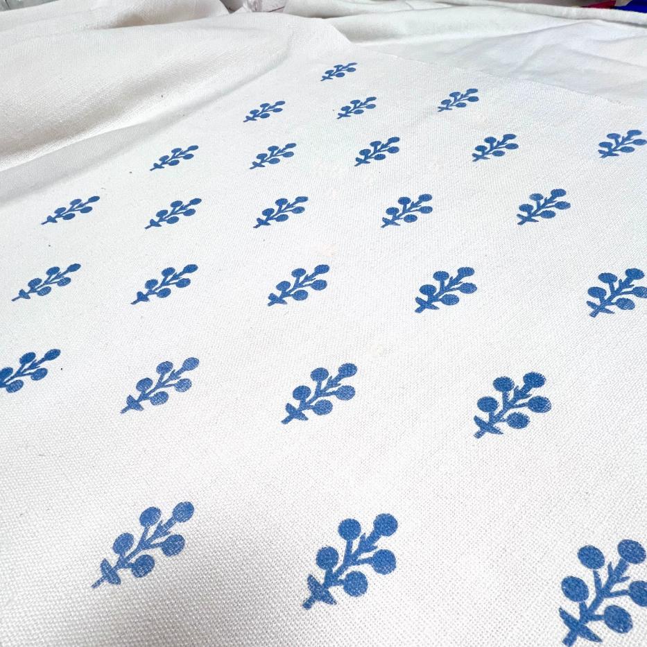 White fabric with a repeating pattern of small, blue, stylized floral or berry motifs spaced evenly across the surface. The texture of the fabric is slightly visible.