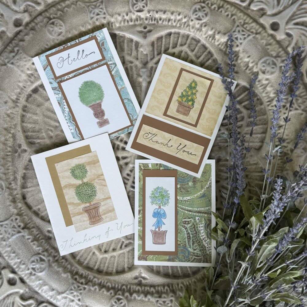 Four greeting cards with hand-drawn topiary designs are arranged on a textured surface with lavender and greenery beside them. Each card says “Hello,” “Thank You,” or “Thinking of You.”.