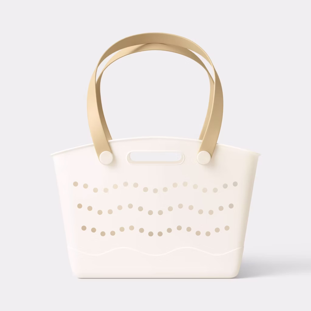 A cream-colored tote bag with tan handles and a pattern of wavy, dotted holes on the side, set against a plain light gray background.