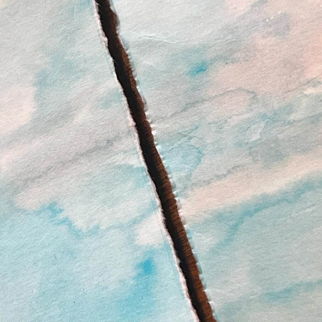 A close-up of two pieces of light blue and white paper with watercolor-like patterns, separated by a rough, uneven tear running vertically through the center.