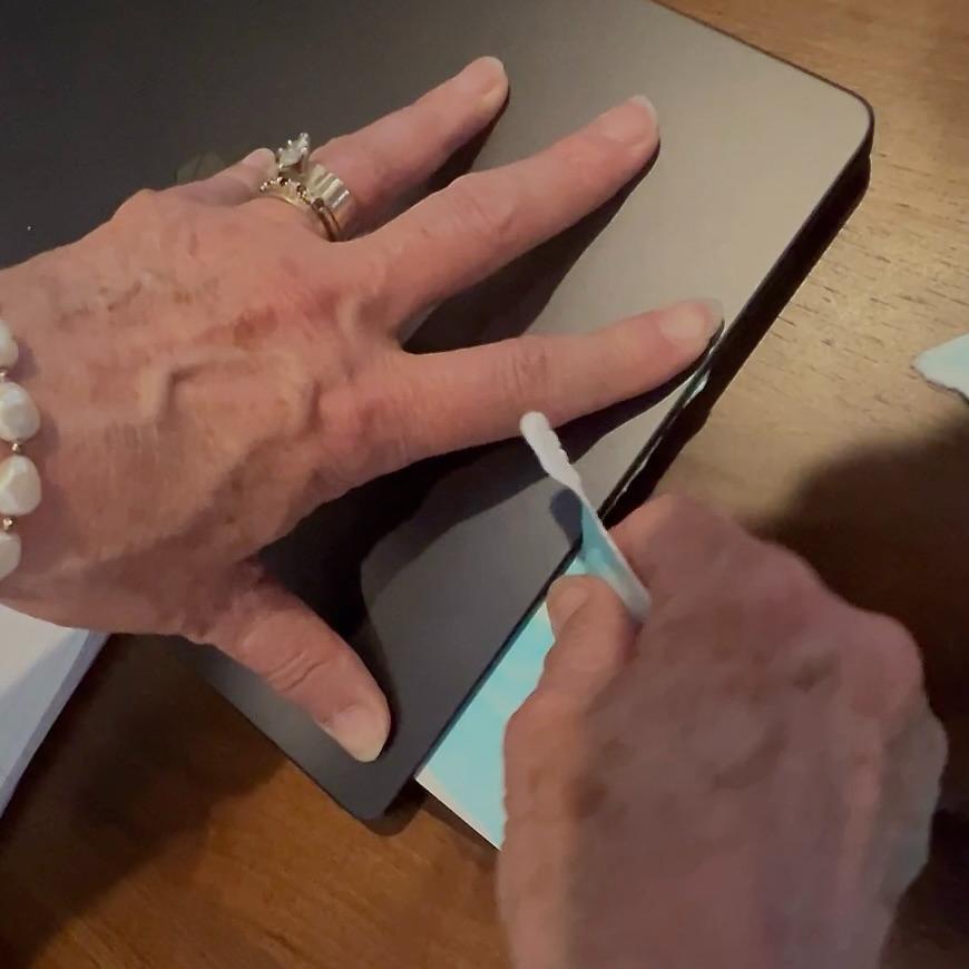 A person holds a piece of painted watercolor paper inside. a closed laptop, pulling the outside edge up against the laptop to tear the paper in a straight line