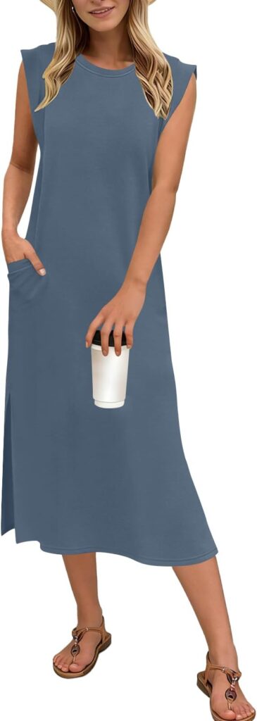 Woman wearing a sleeveless blue midi dress with pockets, holding a white cup in one hand, and wearing brown sandals and a sun hat. She is standing, facing forward, with her hair loose.