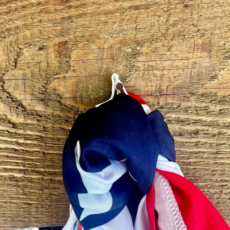 A close-up of an American flag hanging from a small white hook on a rough wooden surface.
