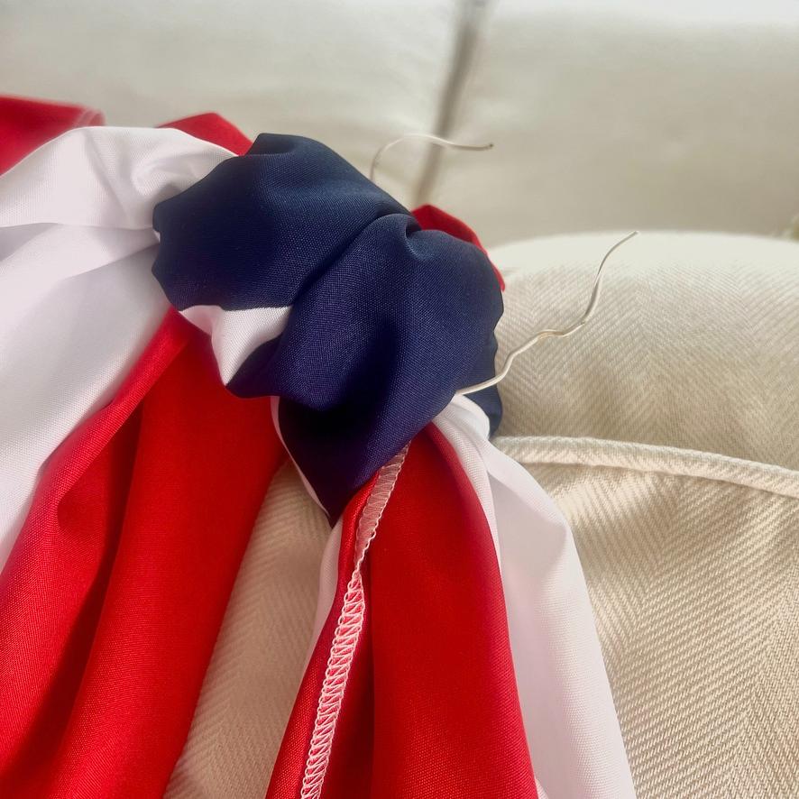 A close-up of a red, white, and blue fabric, possibly a decorative bunting, tied together with thin wire on a cream-colored textured surface.