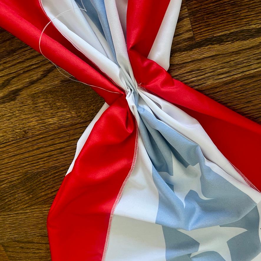 A close-up of a red, white, and blue fabric with stars, resembling part of an American flag, gathered and stitched in the center on a wooden surface.