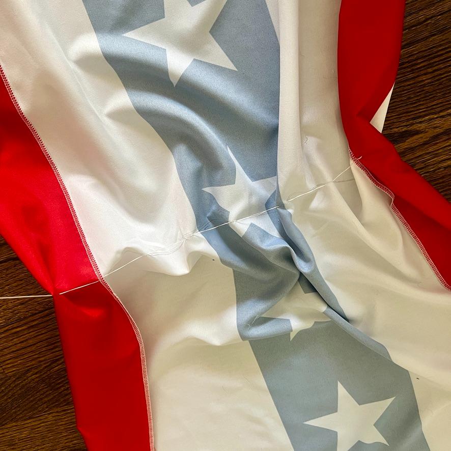 A close-up of a wrinkled American flag lying on a wooden surface, showing red and white stripes with white stars on a blue background.