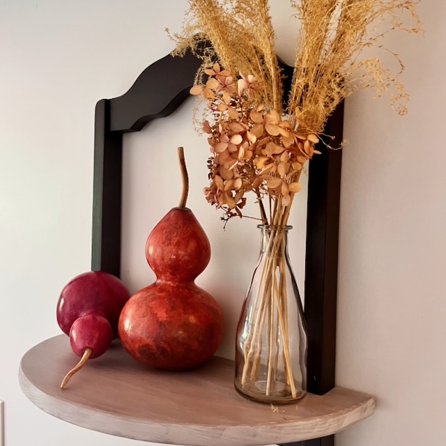 A half-moon wall shelf holds two red gourds and a tall glass vase filled with dried grasses and flowers, set against a light-colored wall—creating an inviting entryway display perfect for greeting guests or inspiring you to make a folding luggage rack for added convenience nearby.