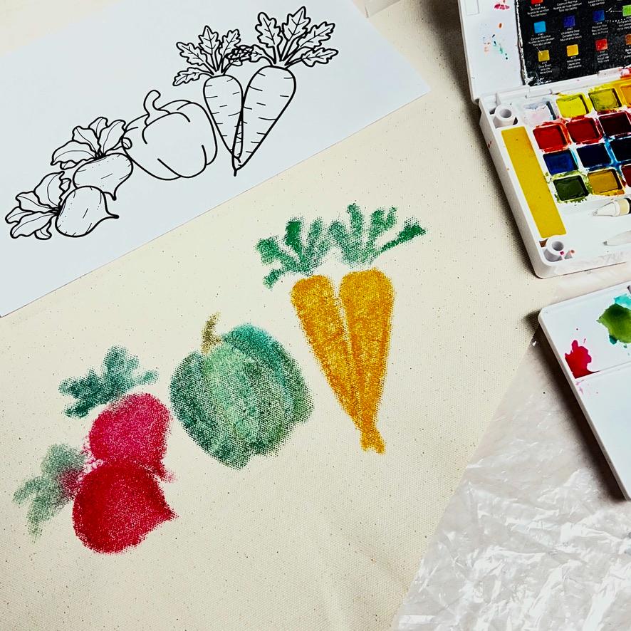 A watercolor set and paper show vegetable outlines, while fabric below displays colorful painted radishes, a green pepper, and two orange carrots mimicking the drawing above.