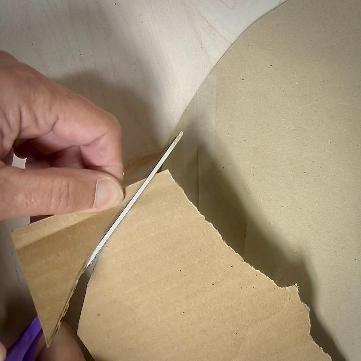 A person uses scissors to cut a piece of brown cardboard on a light-colored surface, creating a unique wreath alternative.