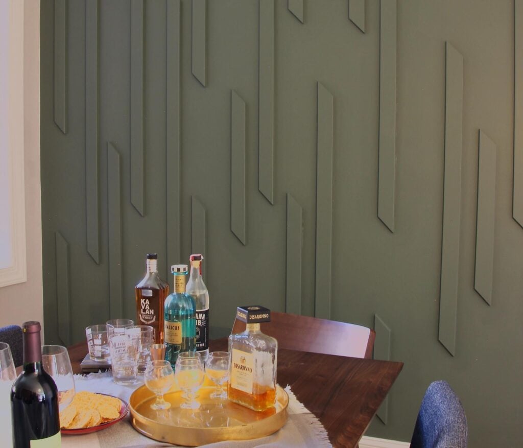 A collection of liquor bottles, glassware, and a plate of crackers on a dining table set against an IKEA Pax closet wall with doors.