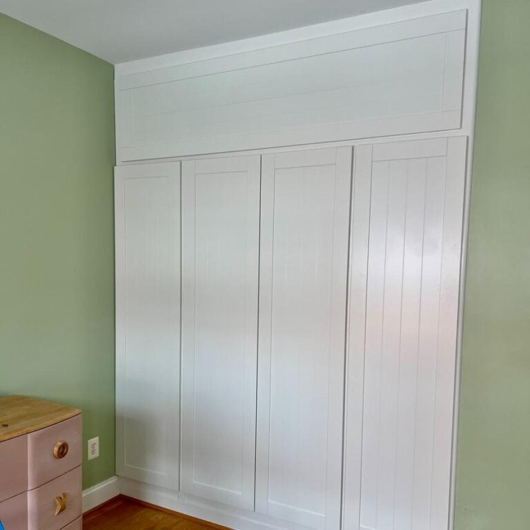 Floor-to-ceiling white built-in cabinets featuring DIY storage above PAX wardrobes, set against a light green wall with vertical paneling.