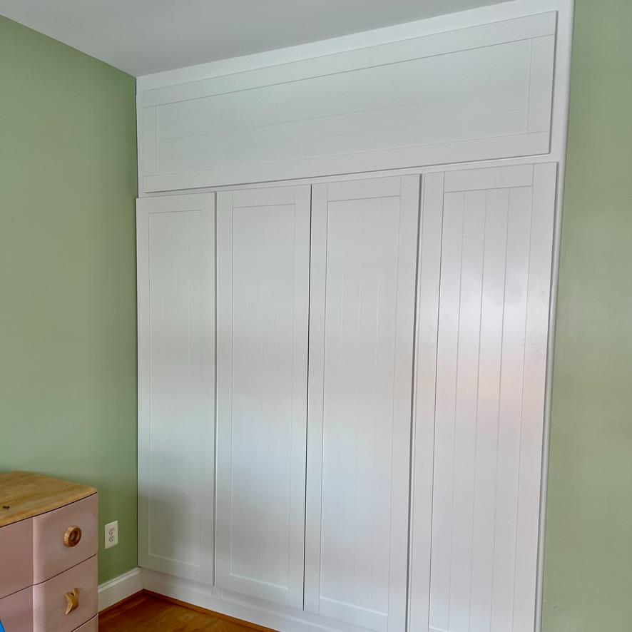 Floor-to-ceiling white built-in cabinets featuring DIY storage above PAX wardrobes, set against a light green wall with vertical paneling.