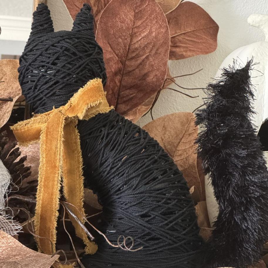 A black rope-wrapped cat figure with a gold velvet ribbon around its neck and a fuzzy black tail.