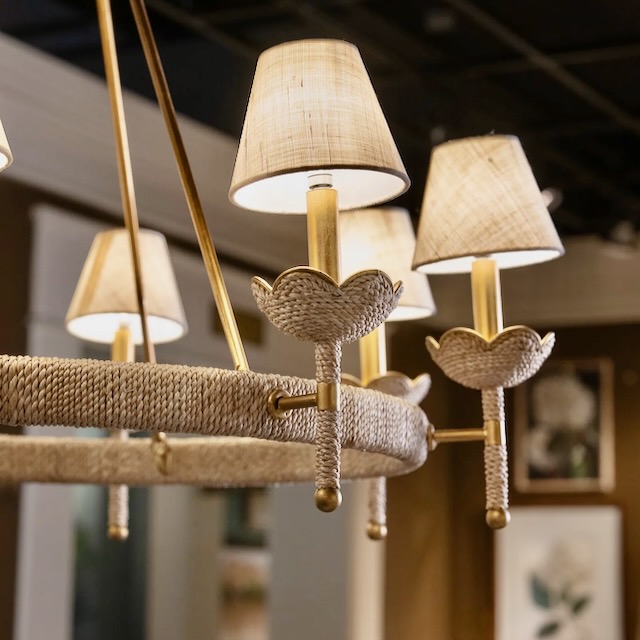 A circular chandelier featuring gold metal arms, rope wrapped lamp detailing, and small fabric-covered lamp shades.