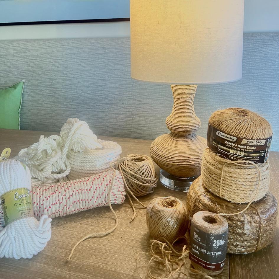 A variety of twine and cord rolls for crafting, including cotton and sisal, arranged on a table next to a rope wrapped lamp.