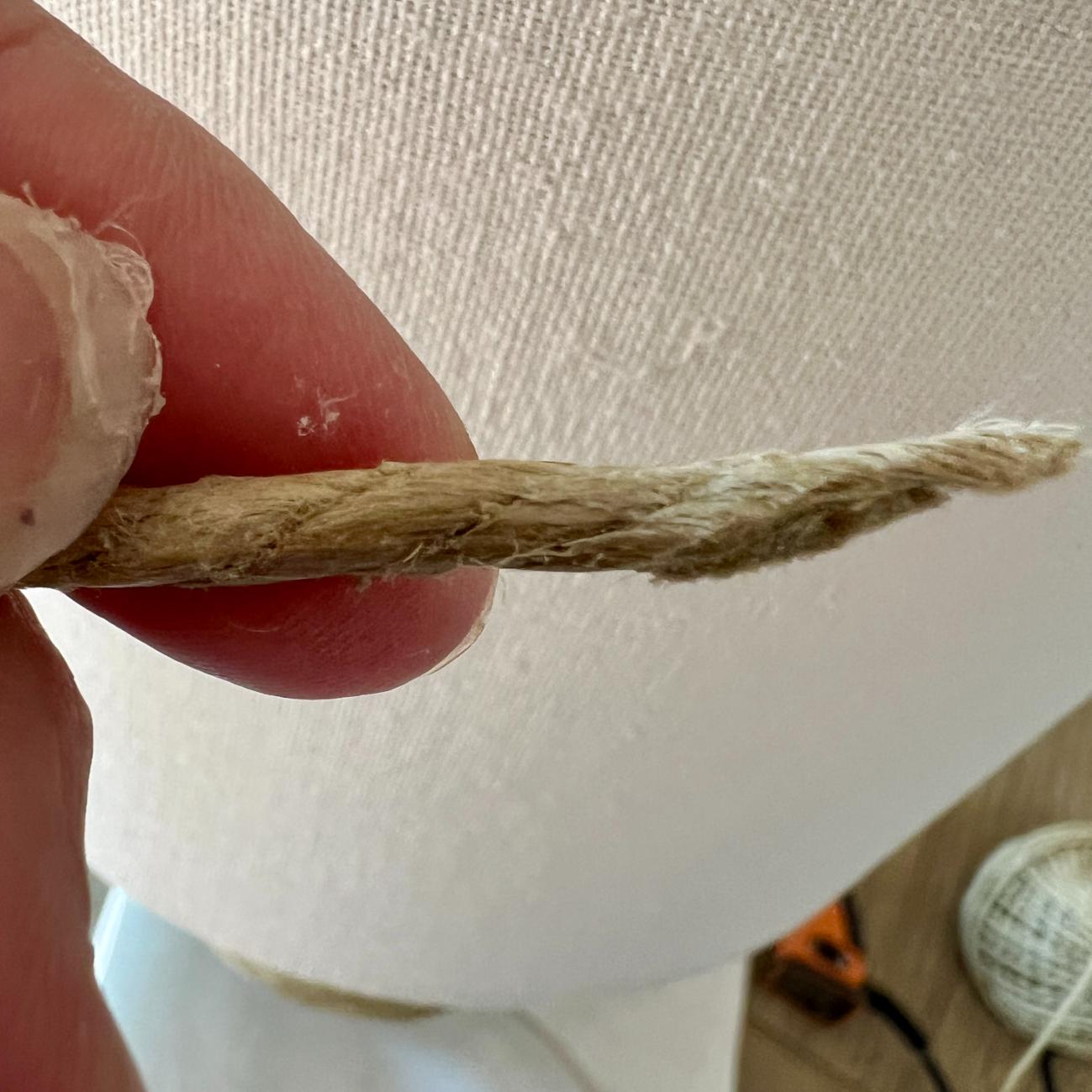 A person’s fingers holding a short length of frayed, natural-fiber twine, similar to the material used for a rope wrapped lamp.