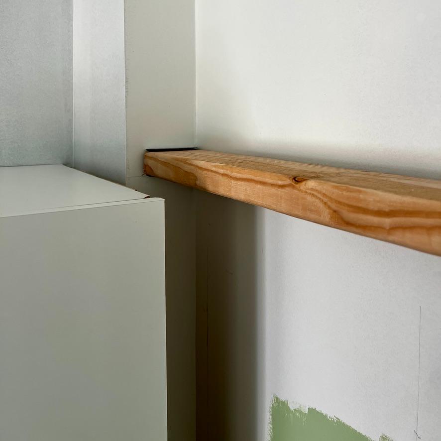 A natural wood shelf mounted to a white wall next to an IKEA Pax closet.