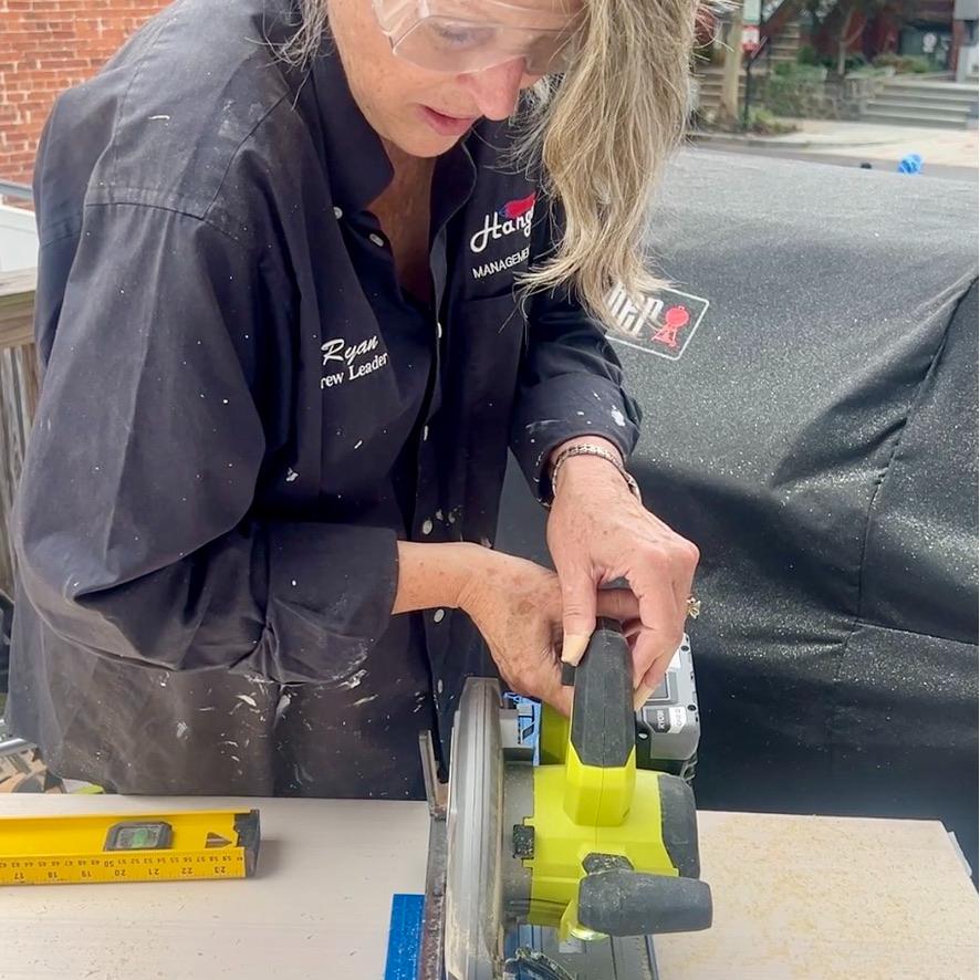 A person wearing safety glasses uses a circular saw to cut a wooden board for an IKEA Pax closet wall, with a yellow level resting nearby.