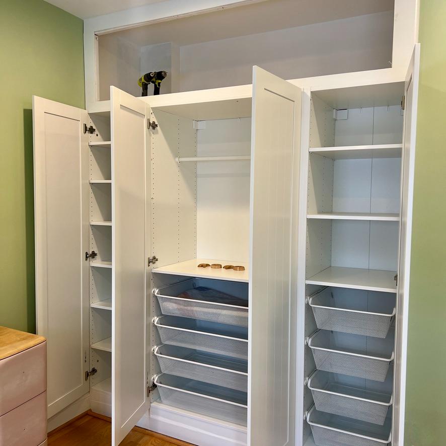 A large white IKEA Pax closet wall with open doors, featuring adjustable shelves, a hanging rod, and pull-out wire drawers.