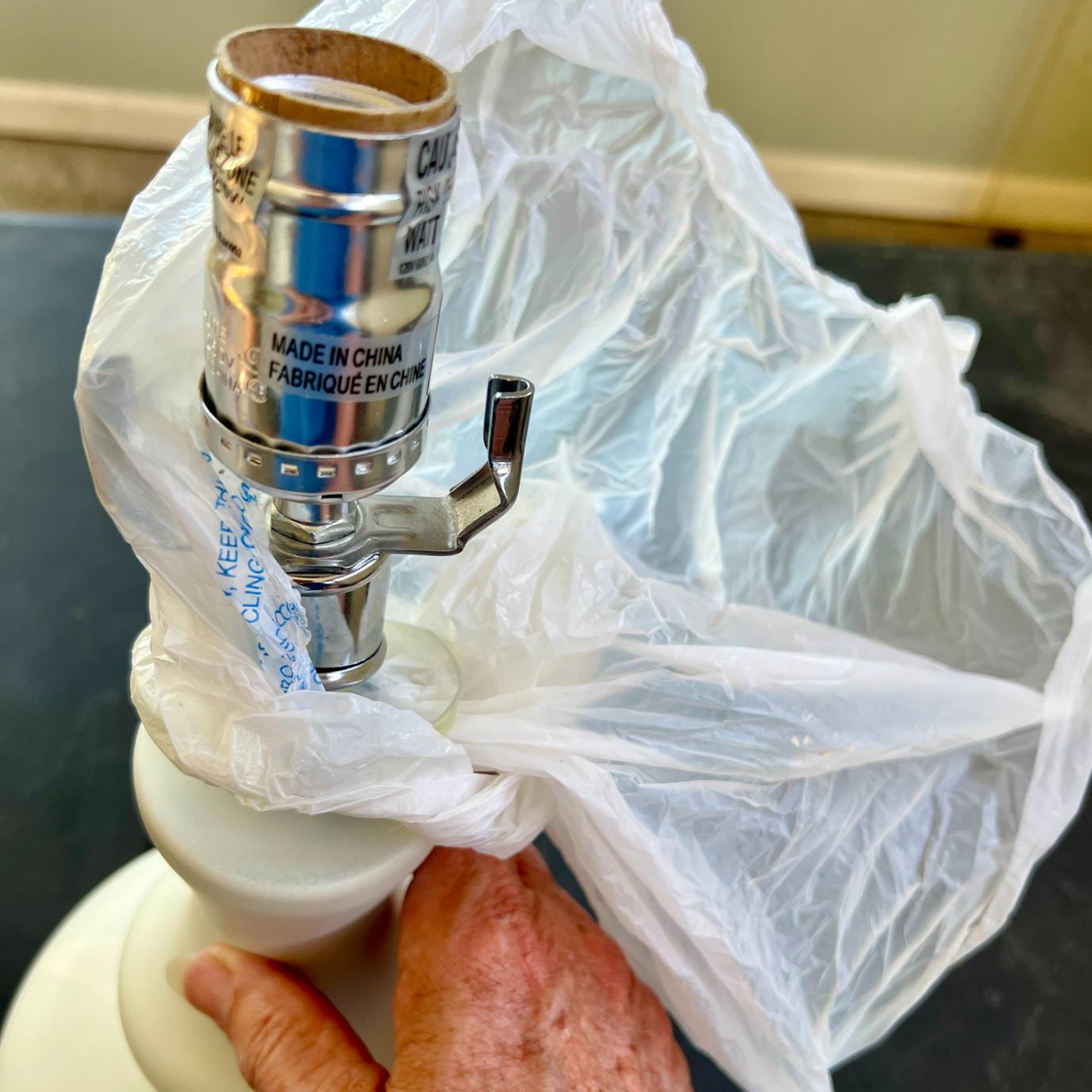 A hand holds a white rope wrapped lamp base covered in protective plastic, showing the metal socket with “Made in China” printed on the side.