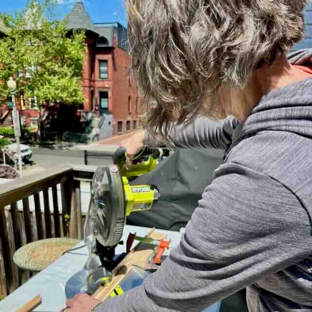 A person uses a circular miter saw to cut wood for DIY storage above Pax wardrobes on an outdoor deck.