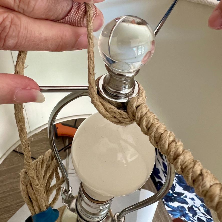 Hands wrap jute rope around the base of a rope wrapped lamp finial and its metal support frame.